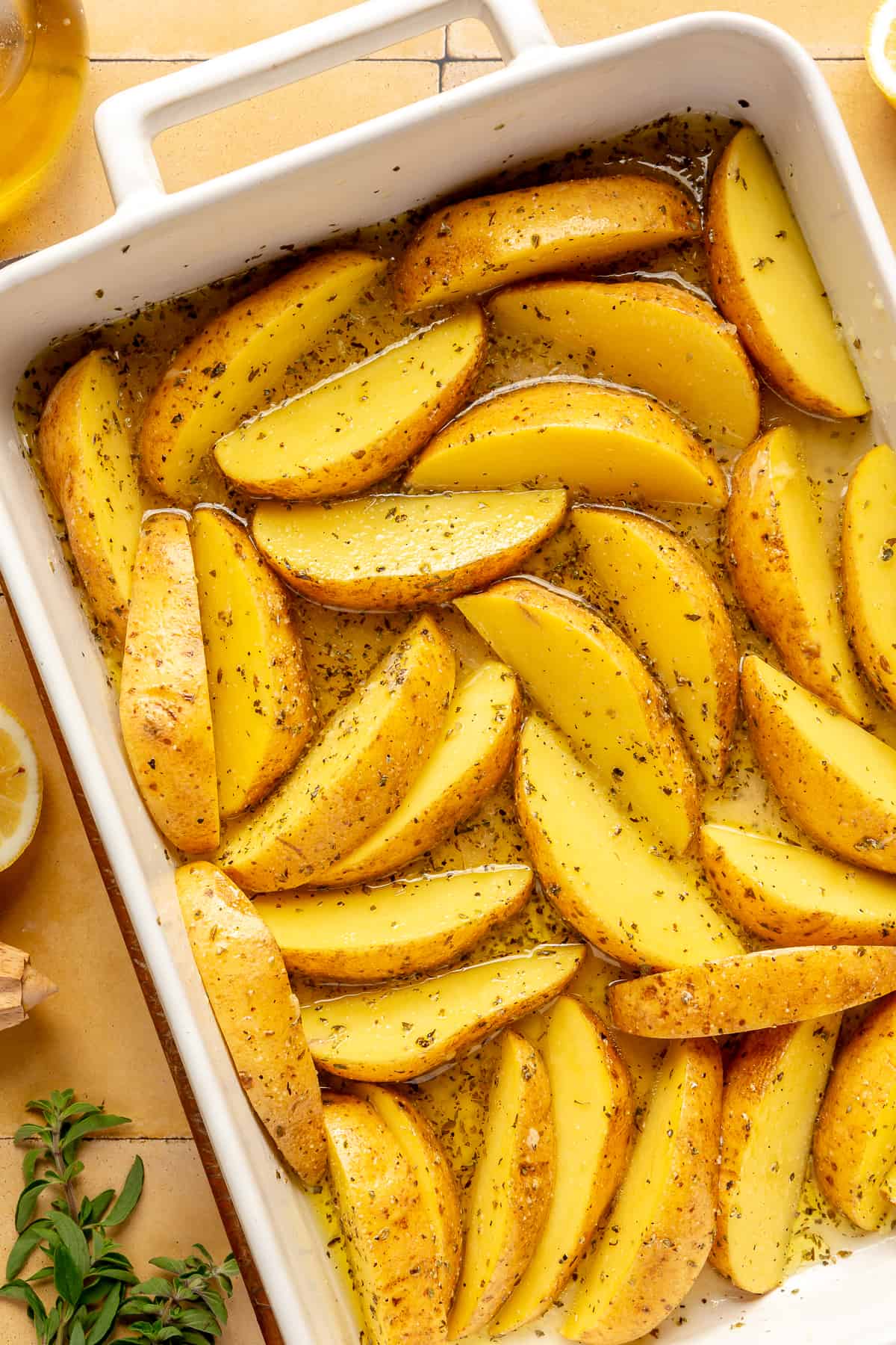 Potato wedges in white baking dish with all other ingredients mixed in.