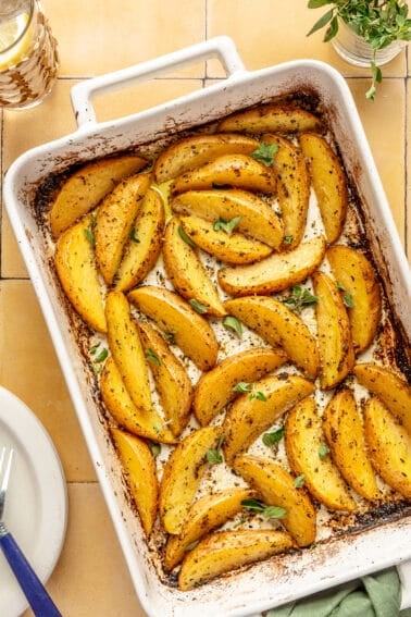 Greek-Style Potatoes baked in white baking dish. Herbs on top.