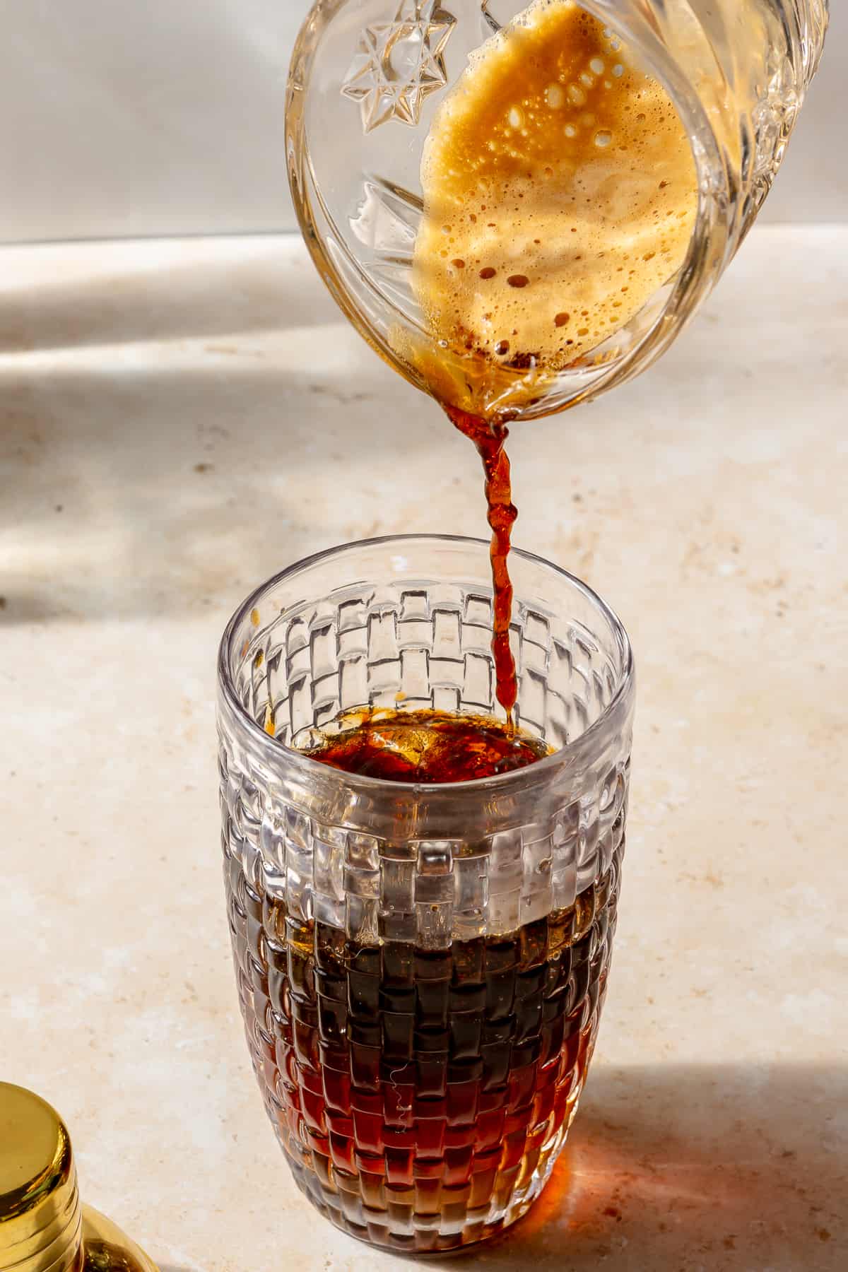 Espresso pouring into glass cocktail shaker with other ingredients.
