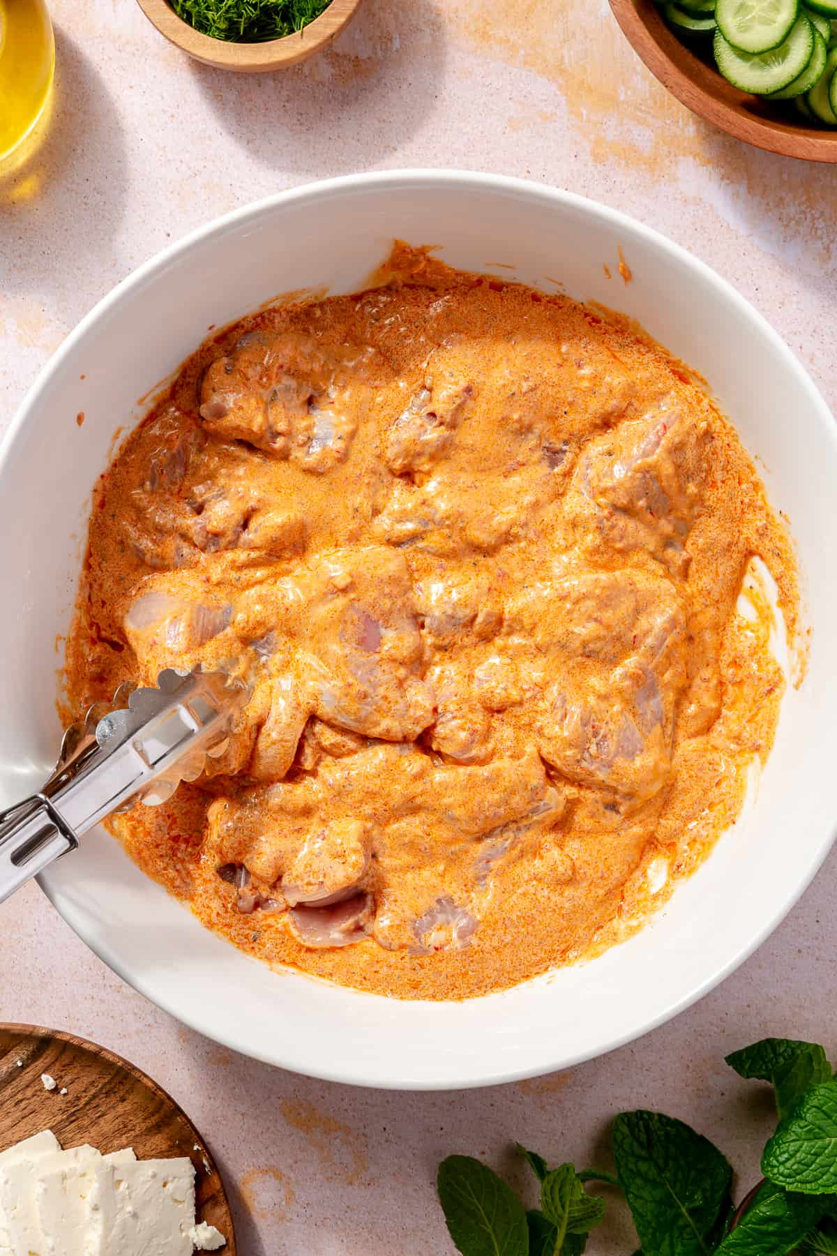 Raw chicken in harissa-yogurt marinade in large white bowl.
