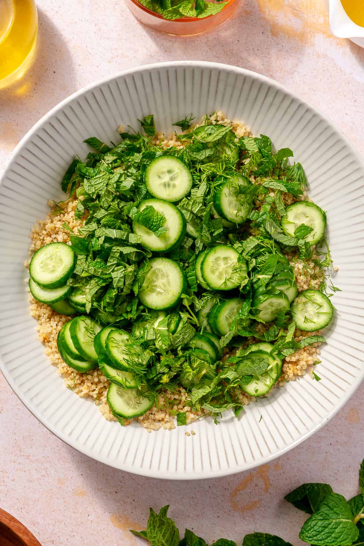 Cooked quinoa topped with herbs and cucumbers. Not combined.