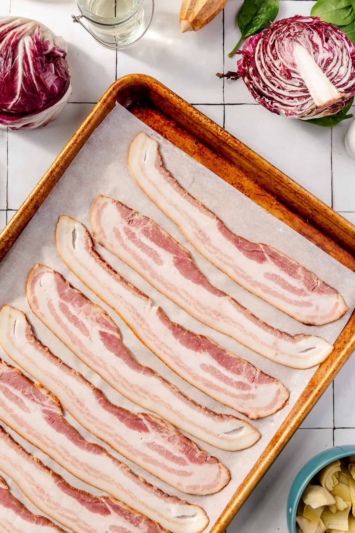 Raw bacon on a sheet pan lined with parchment paper. Other ingredients scattered around.