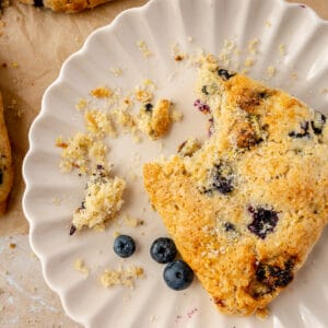 One scone on plate with bite taken out of it and crumbs.