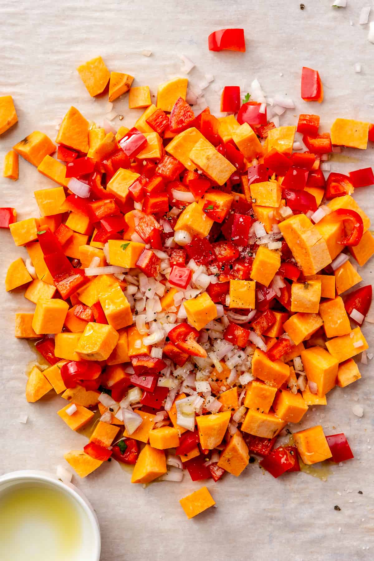 Diced sweet potato, bell peppers, and shallot piled on a parchment-lined sheet pan.