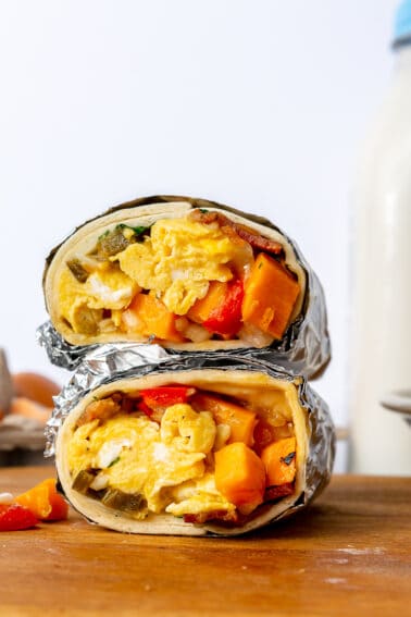 Two burritos wrapped in foil and cut in half then stacked on top of each other.
