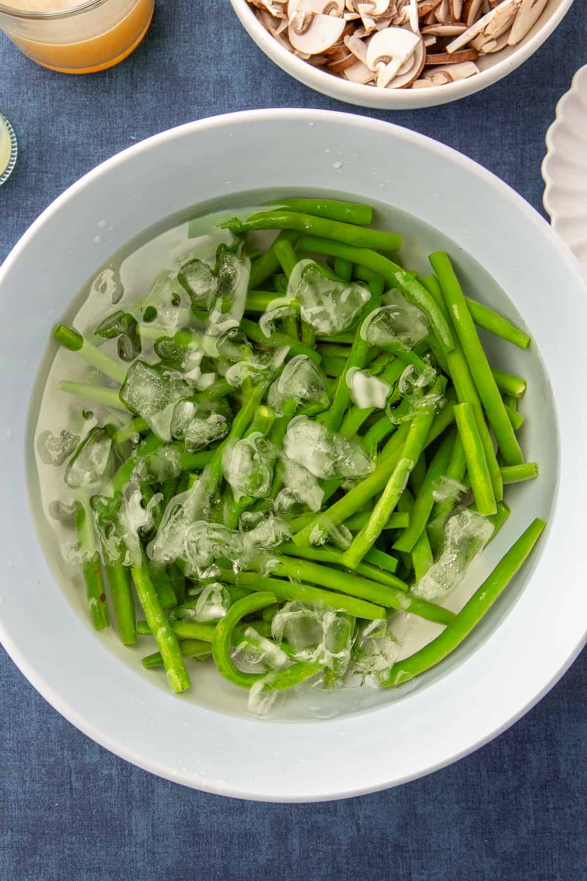 Par-cooked green beans in an ice bath in a large white bowl.