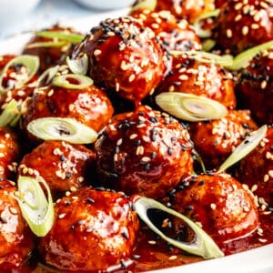 Close up of Korean-Inspired BBQ Chicken Meatballs on white platter. Meatballs garnished with sesame seeds and green onions.