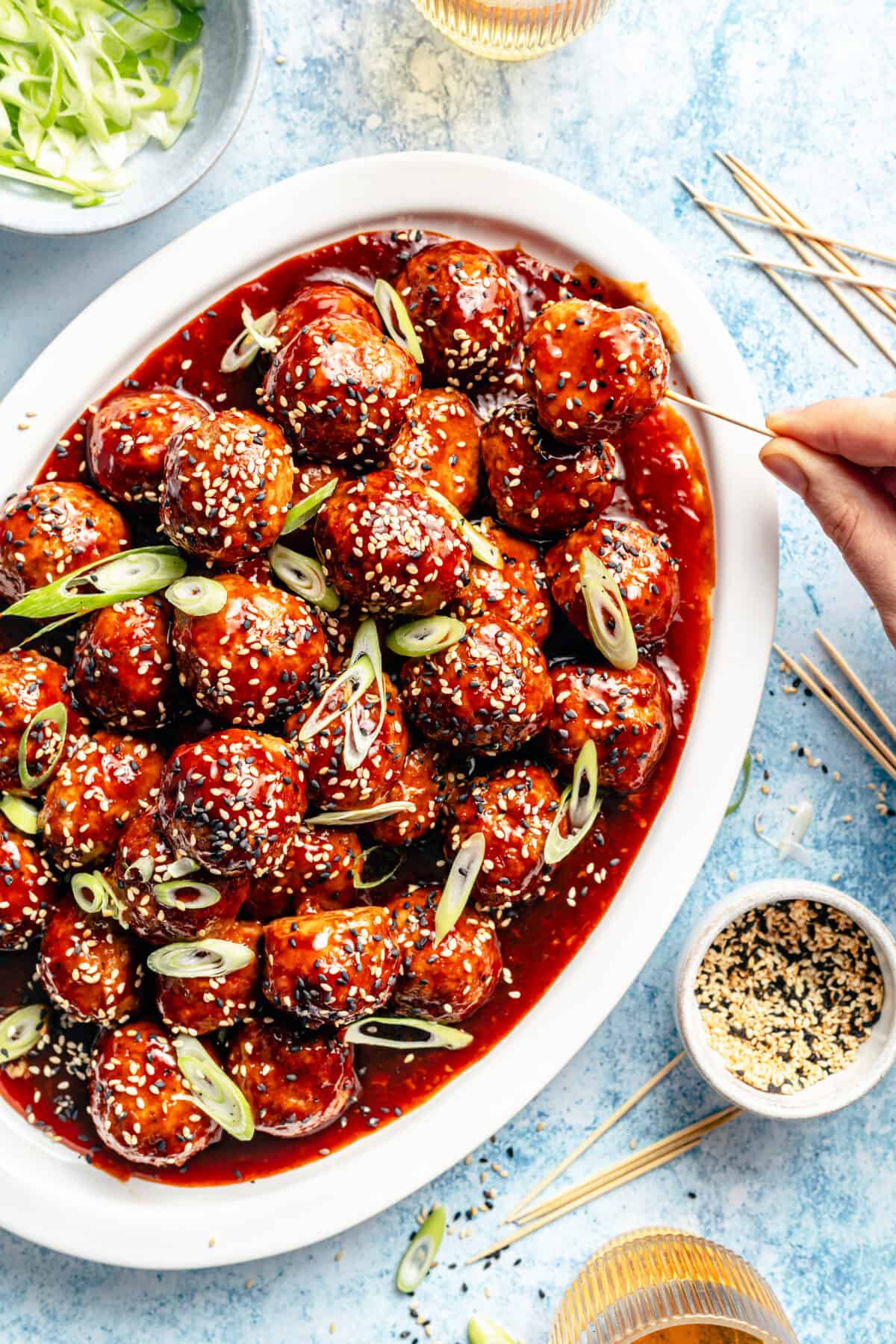 Platter of Korean-Inspired BBQ Chicken Meatballs with hand holding toothpick reaching in.
