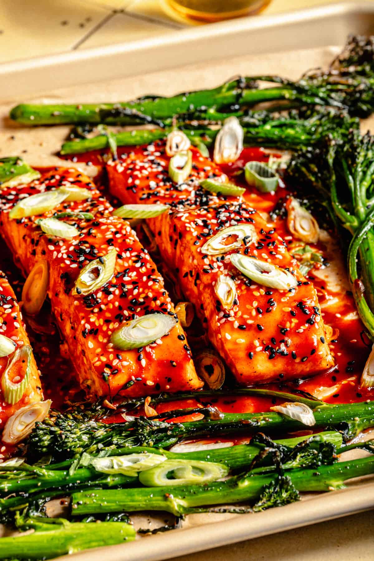 Close up of Gochujang Glazed Salmon and broccolini on a sheet pan with sliced green onions on top.