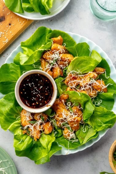 Four Honey-Garlic Chicken Lettuce Wraps on a round plate with a small bowl of extra sauce.