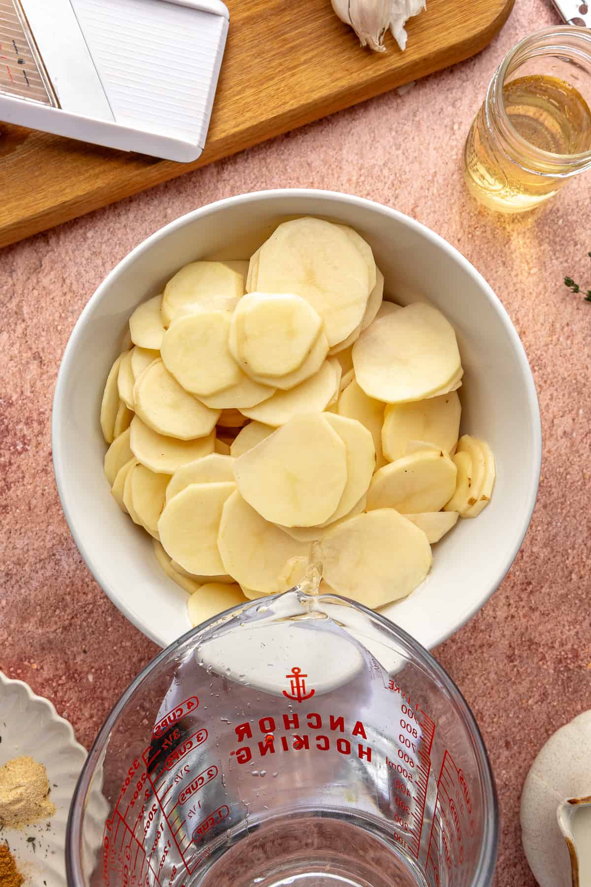 Sliced potatoes in a large white bowl. Water being poured into it.