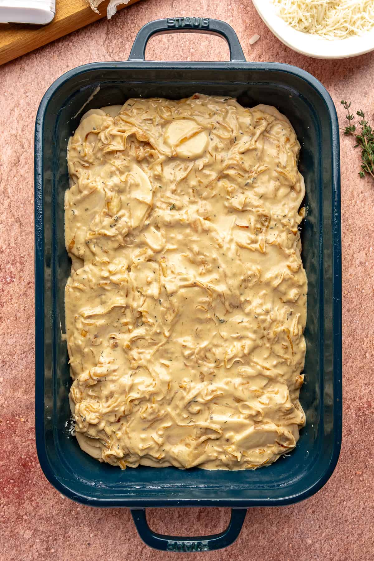 Uncooked Caramelized Onion Scalloped Potatoes in a blue baking dish.