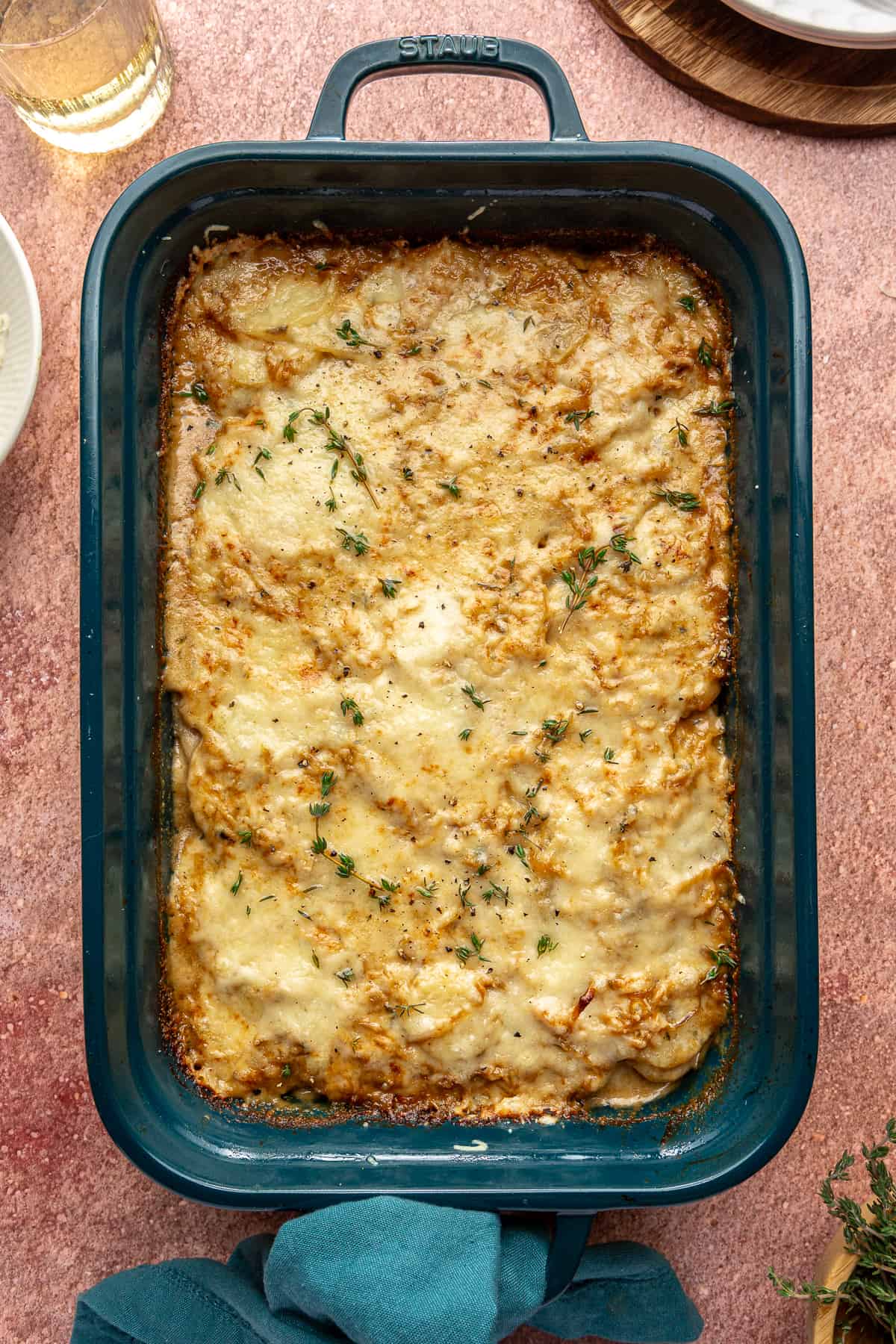 Blue baking dish of Caramelized Onion Scalloped Potatoes on red backdrop.
