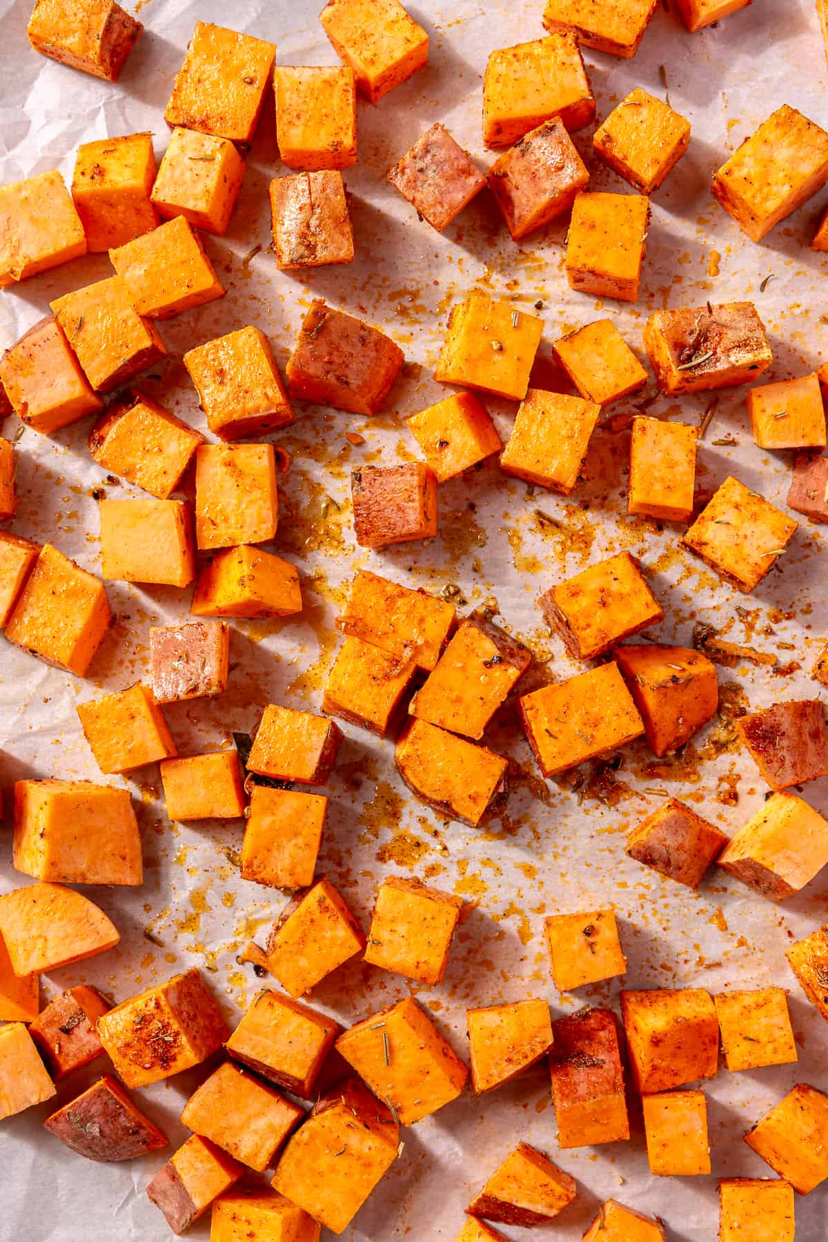 Diced sweet potatoes on a baking sheet with seasoning on top.