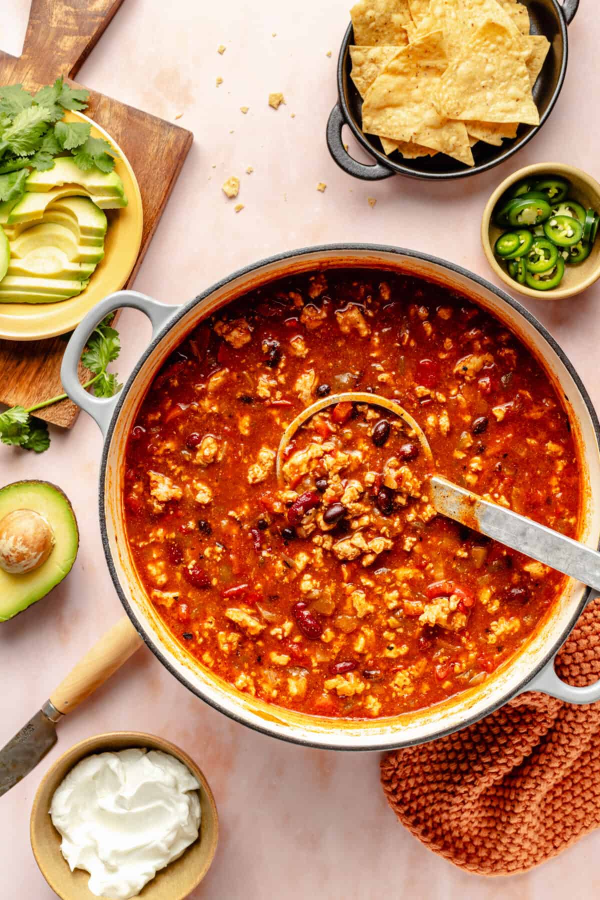 Large pot of Chicken Enchilada Chili with ladle in it. Garnishes scattered around.