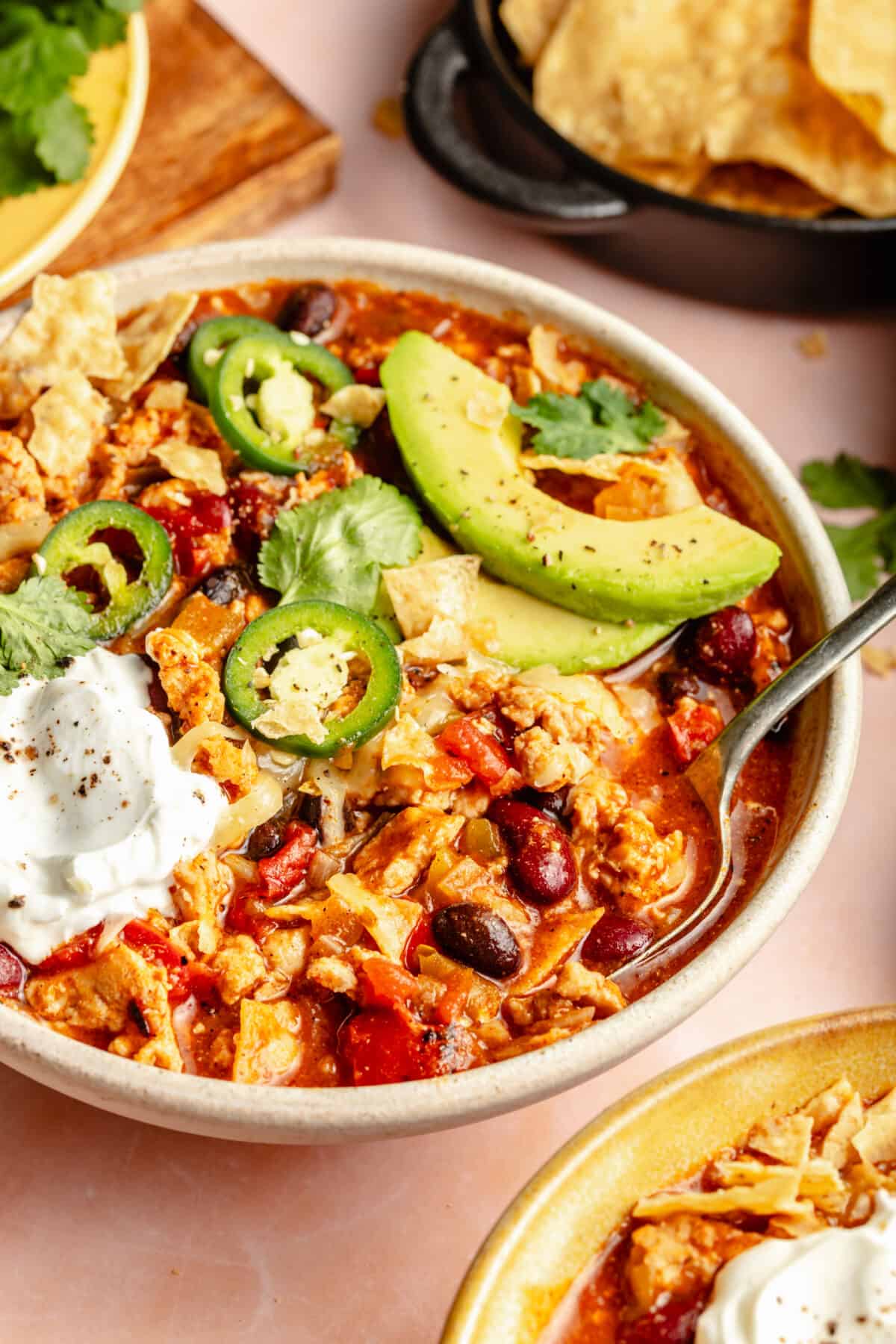 Bowl of Chicken Enchilada Chili garnished with cheese, avocado, sour cream and jalepenos.