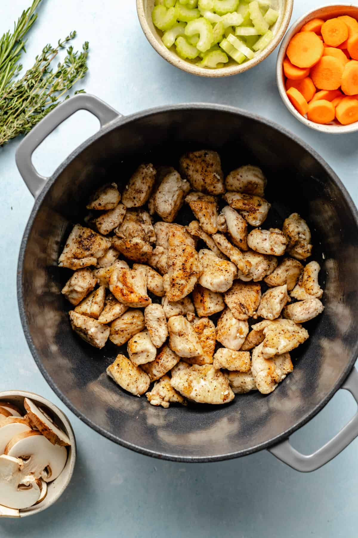 Cut chicken browned in large, dark dutch oven.. Bowls of celery and carrots in the corner of the photo.