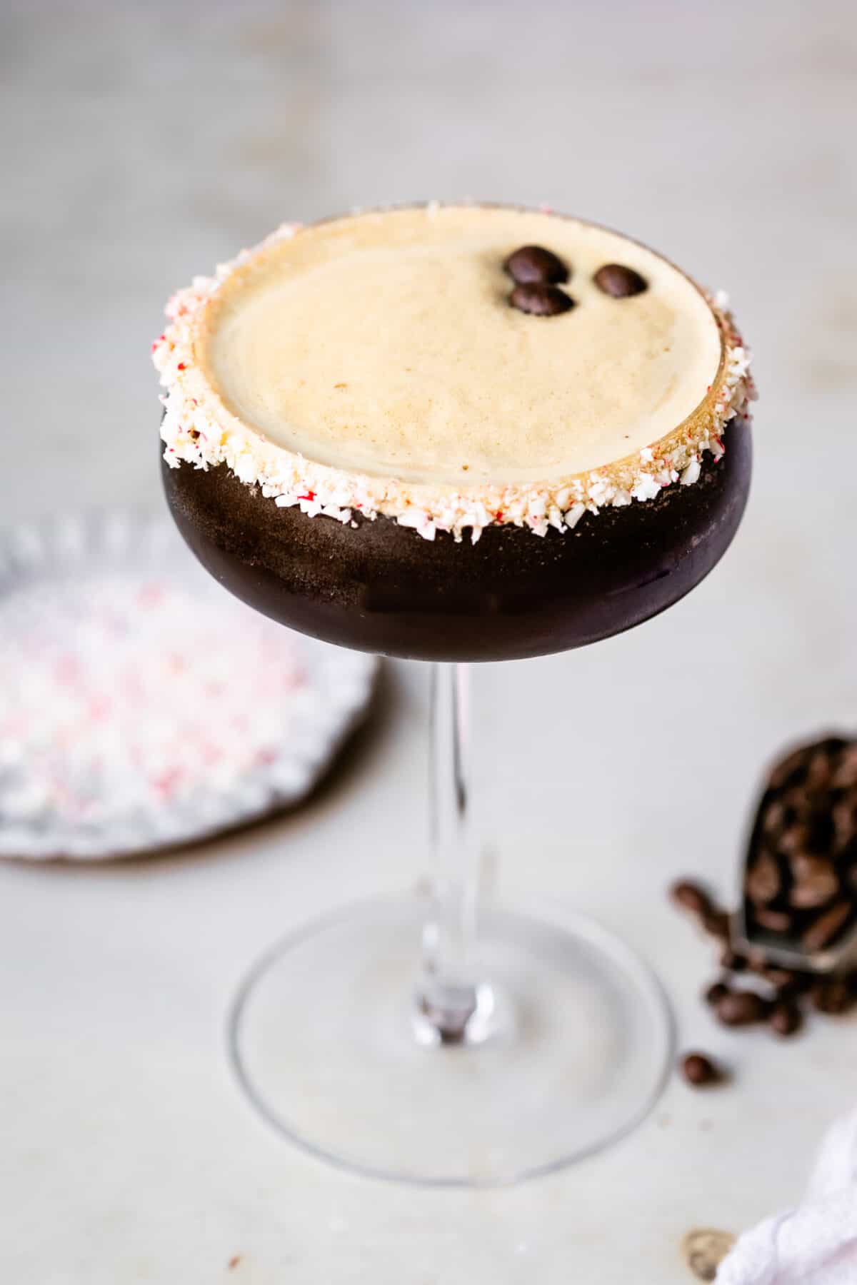 Peppermint Espresso Martini in a tall glass. Espresso beans and crushed peppermint in the background.