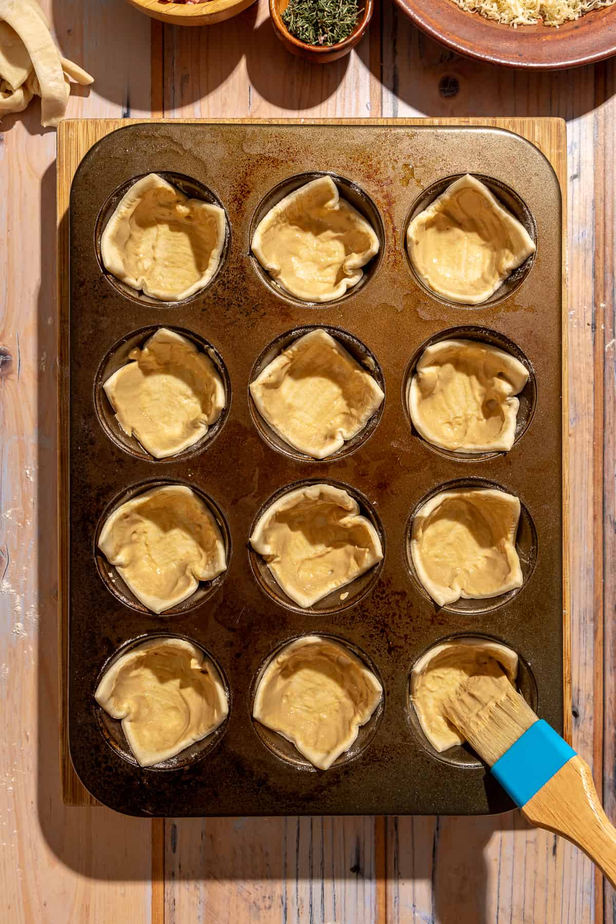 Puff pastry in muffin tin openings. Patry brush with Dijon mustard being brushed onto puff pastry.