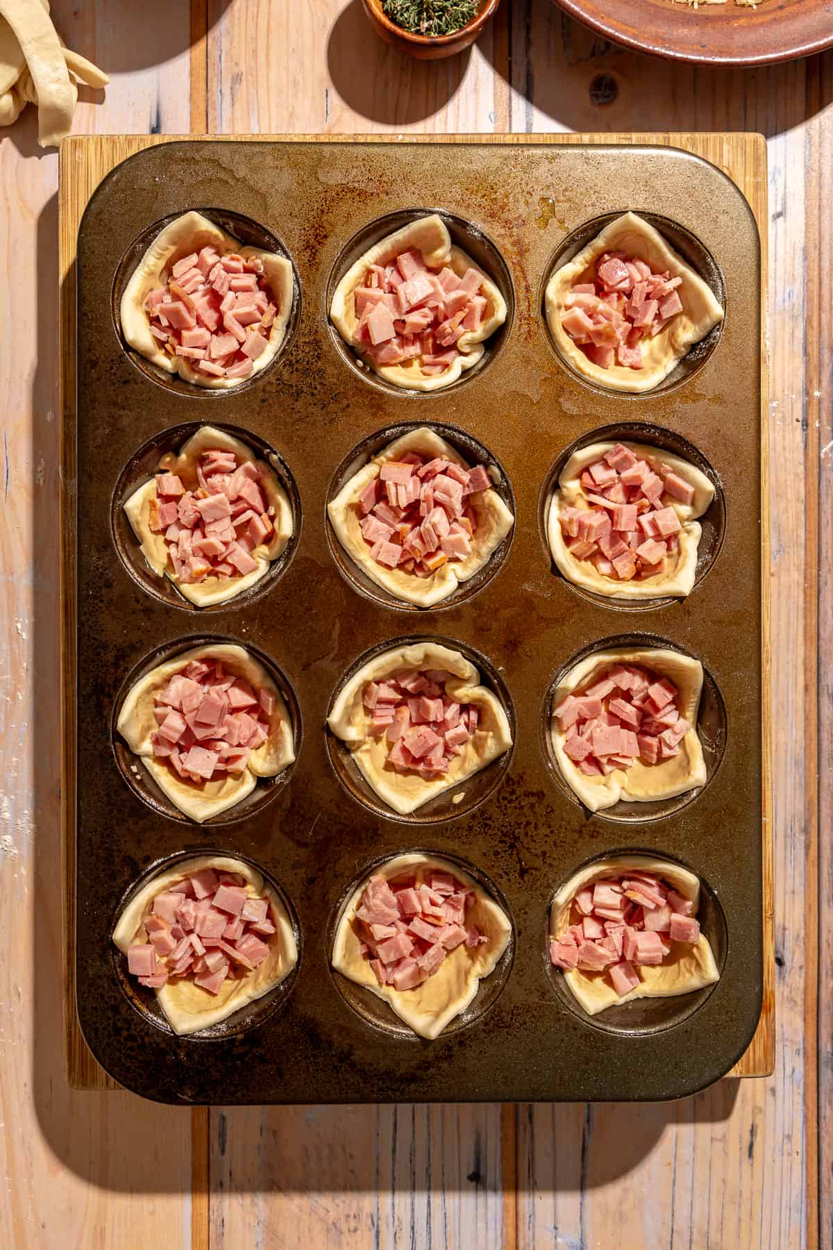 Raw puff pastry in muffin tin filled with diced ham.
