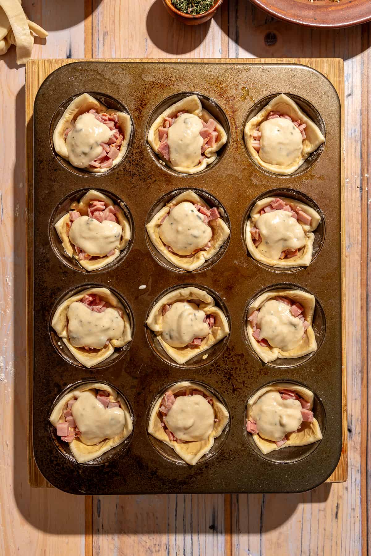 Raw Mini Croque Monsieur Bites being assembled. Puff pastry filled with ham and topped with bechamel.