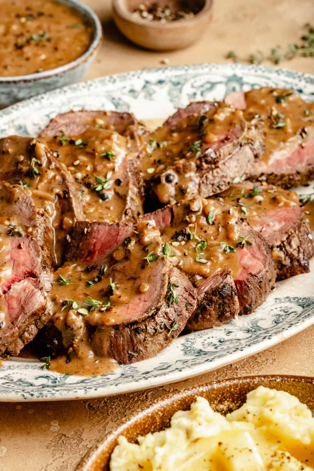 Close up of Beef Tenderloin sliced on large oval platter with Au Poivre on top.