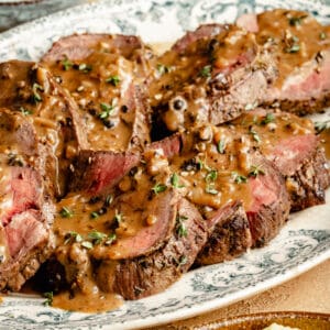 Close up of Beef Tenderloin sliced on large oval platter with Au Poivre on top.