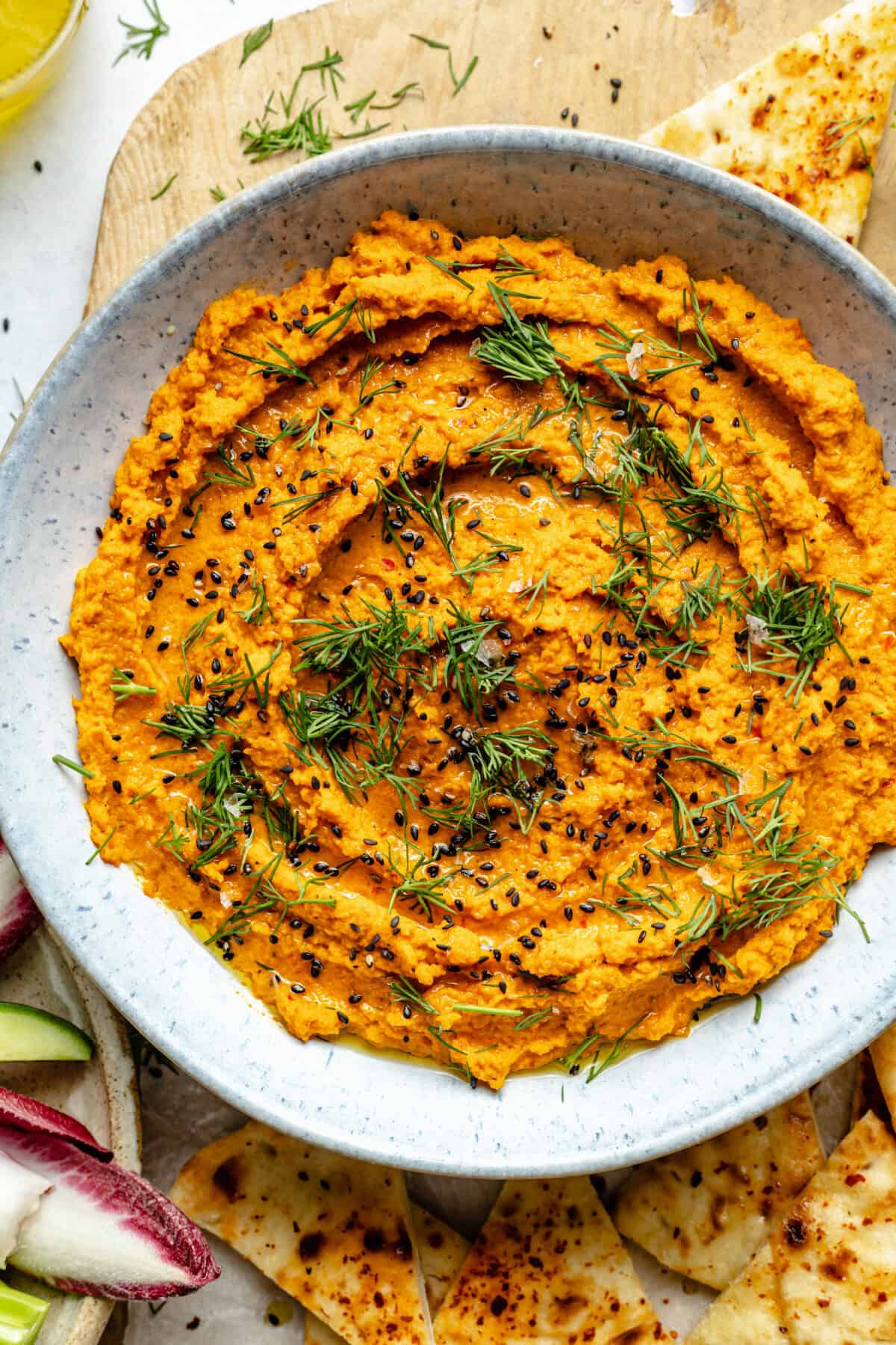 Close up of Harissa Carrot Dip in bowl. Dill and black sesame seeds on top.