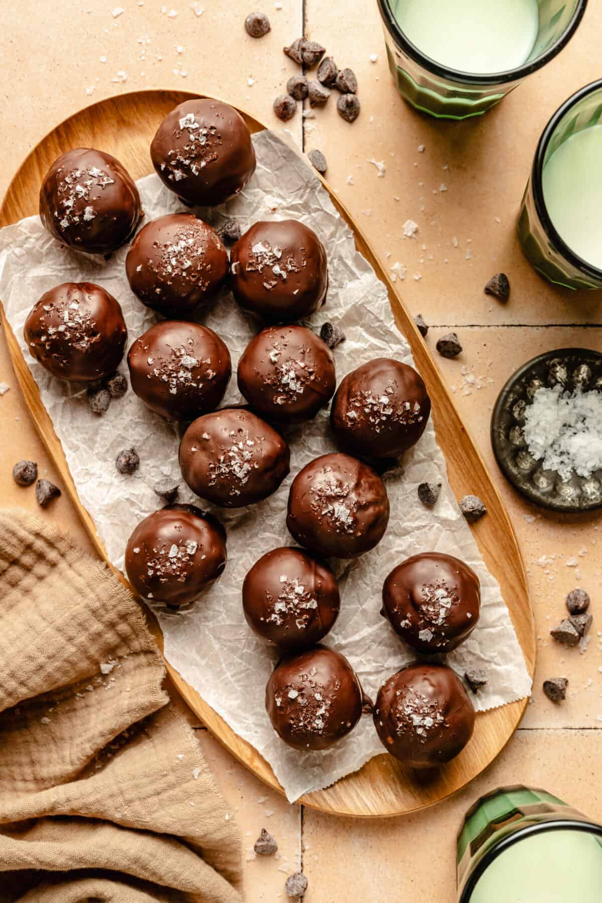 Thin Mint Energy Bites on a large platter. glasses of milk around. Chocolate chips and flaky salt scattered around.