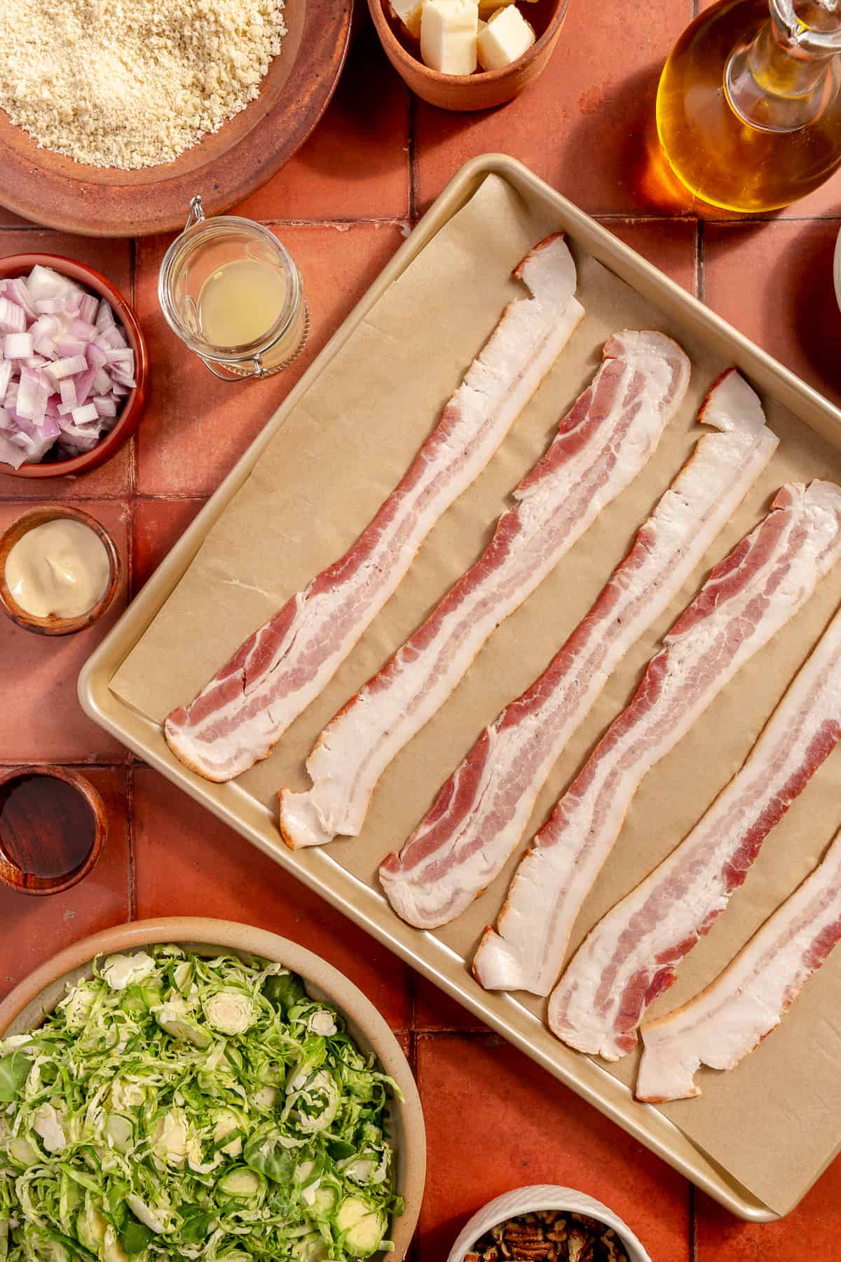 Raw bacon on sheet pan lined with parchment paper. Other ingredients scattered around.
