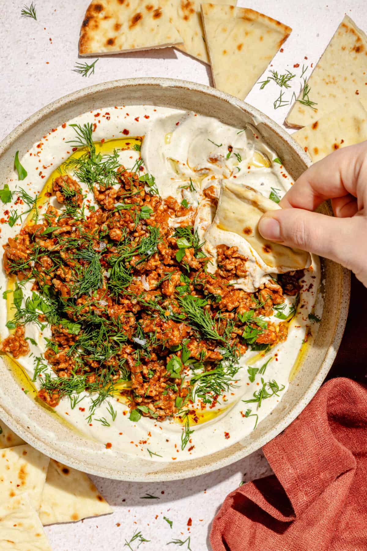 Spicy Lamb and Eggplant Labneh in a low bowl. Hand dipping pita into bowl.