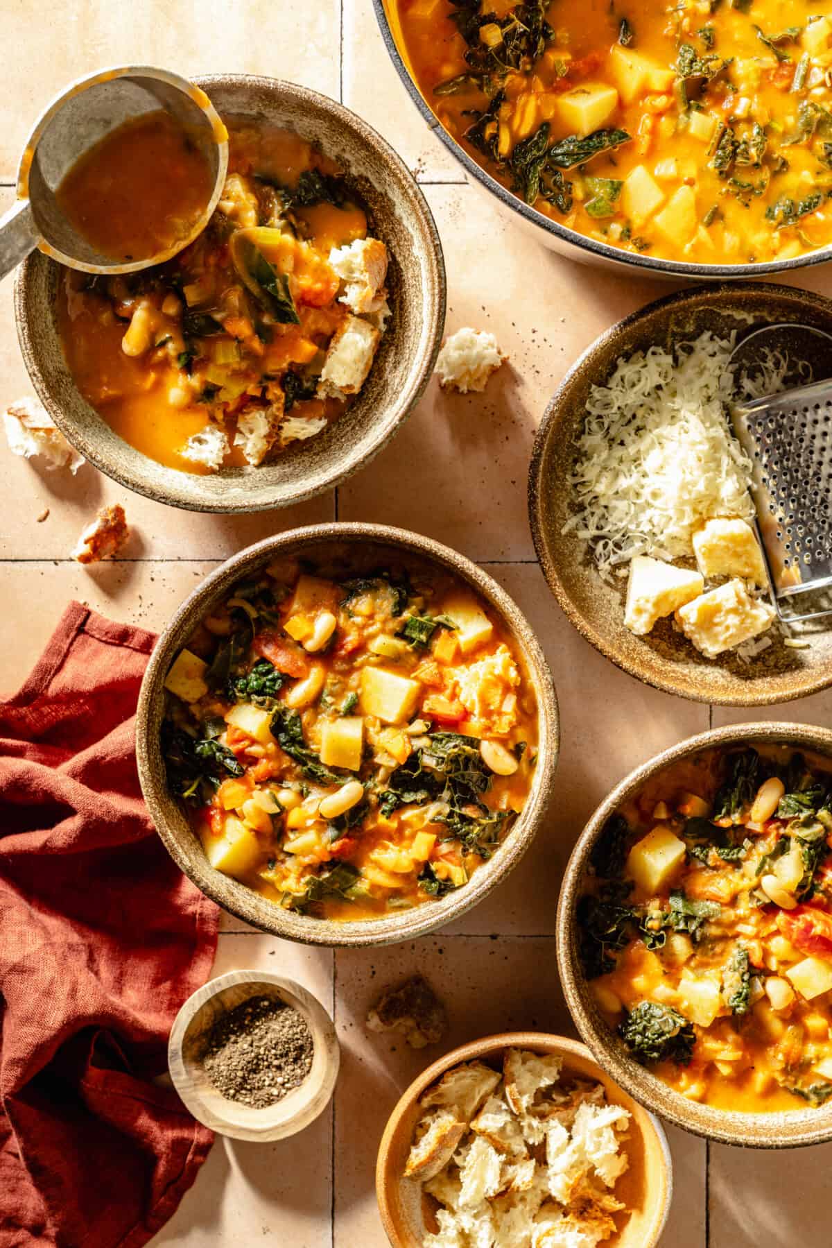 Tuscan Ribollita in three bowls. Toppings in bowls scattered around.