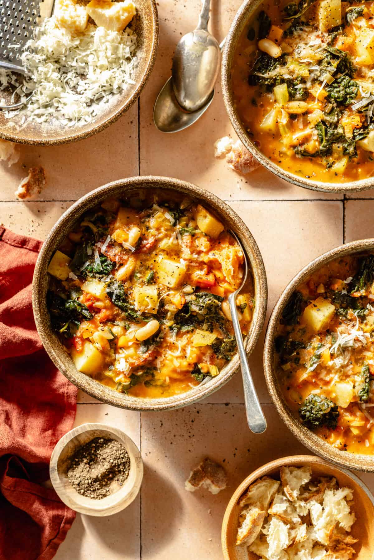 Tuscan Ribollita in three bowls. Toppings in bowls scattered around.