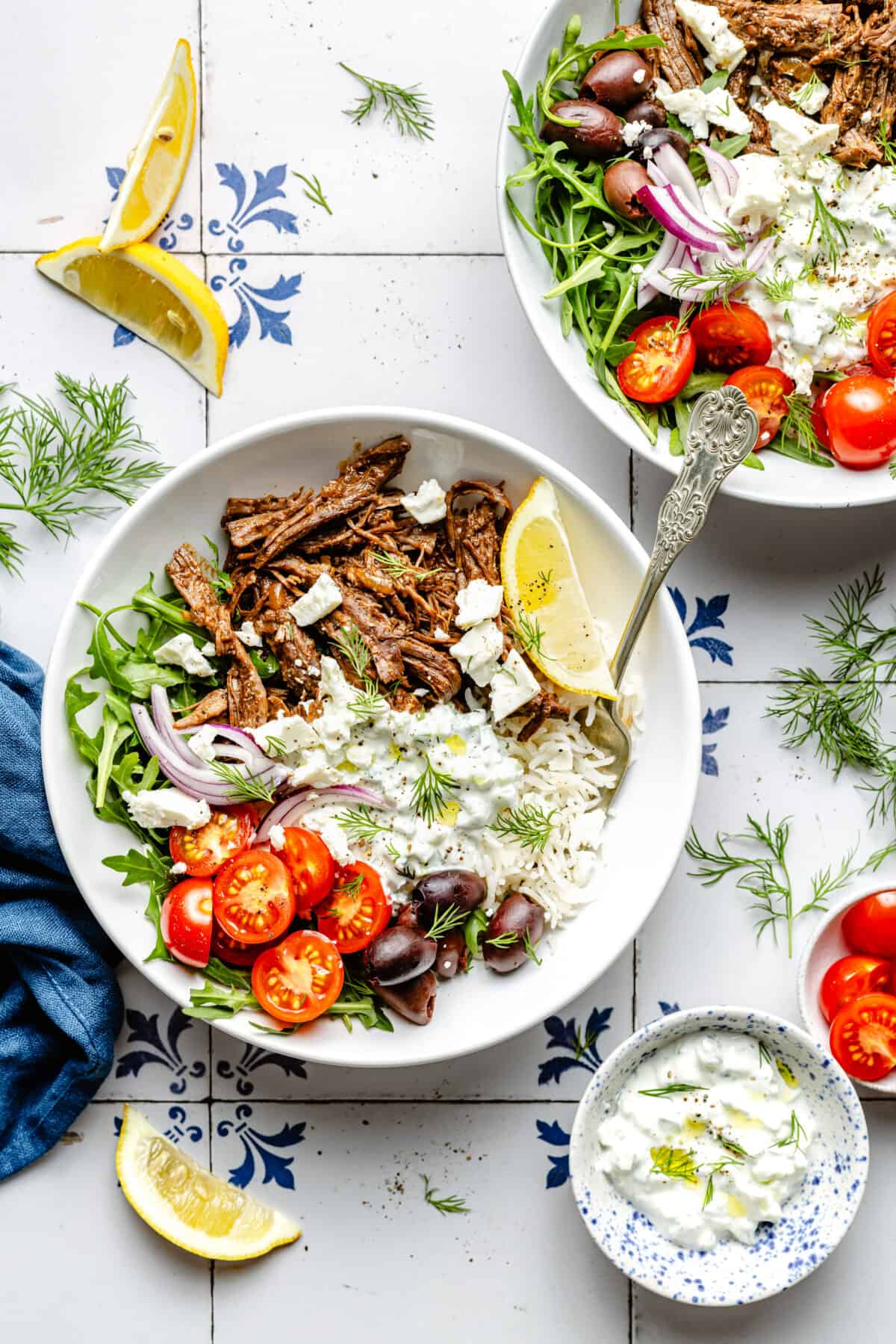 Instant Pot Shredded Greek Beef in bowl with garnishes scattered around.