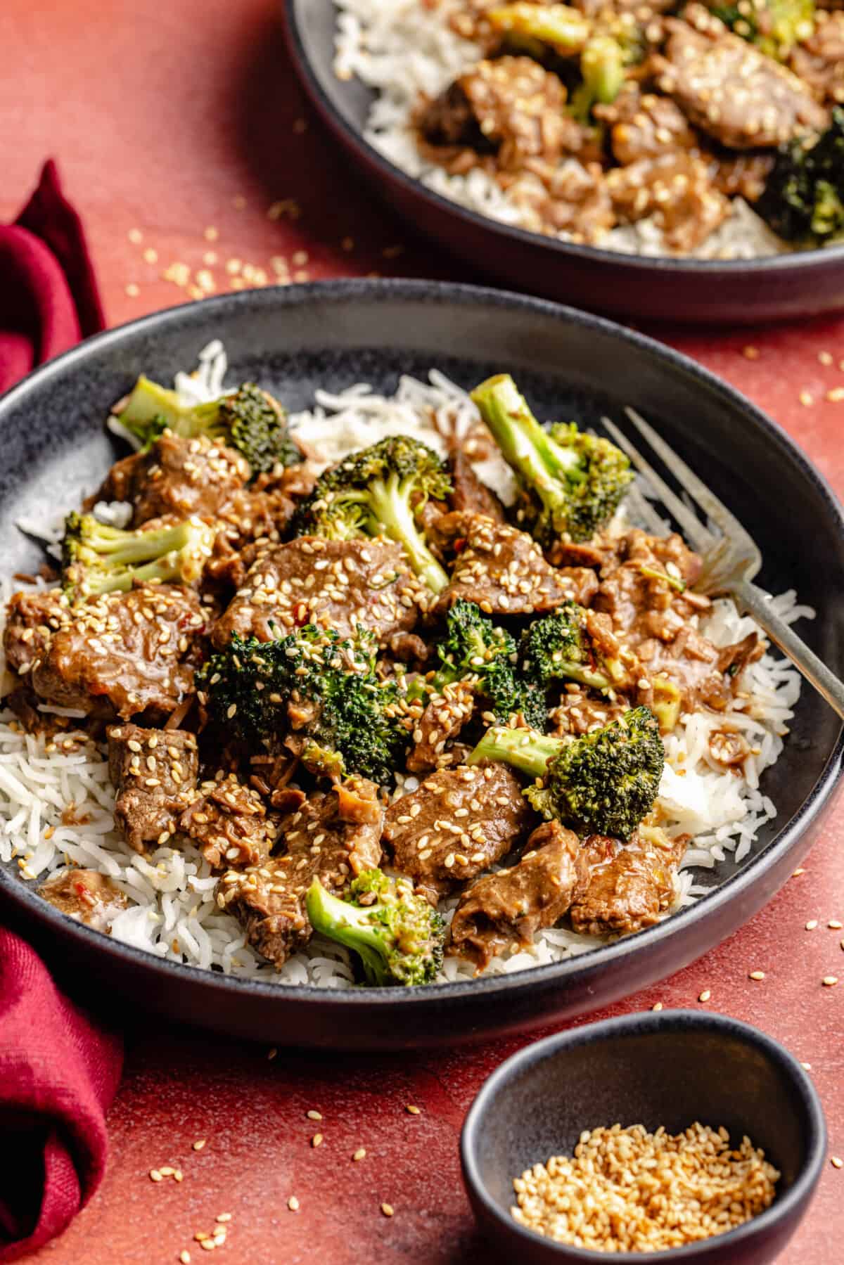 Slow Cooker Beef and Broccoli in bowls on red backdrop.