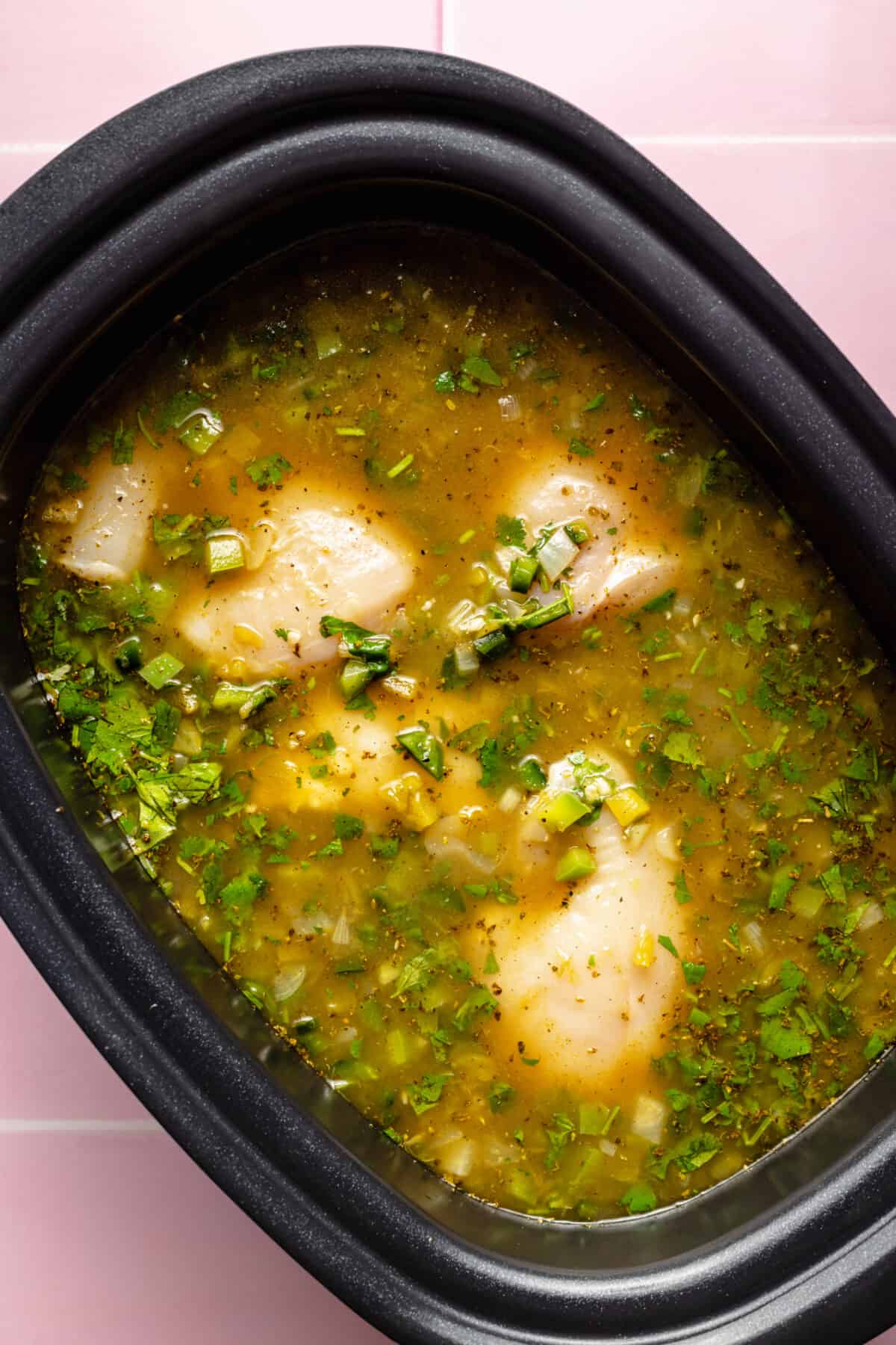 Raw chicken, broth, and other ingredients in slow cooker.