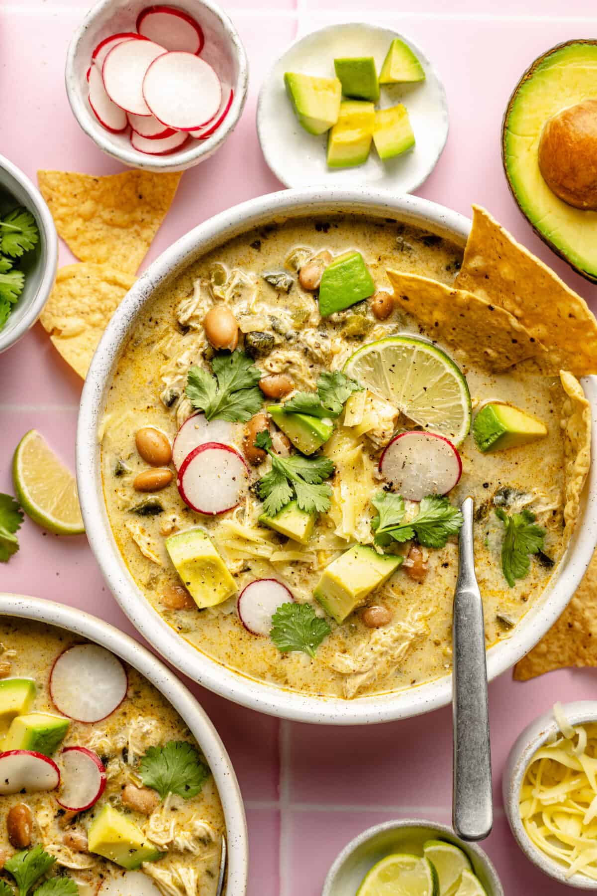 Slow Cooker Green Enchilada Chicken Soup in two bowls. Garnishes scattered around.
