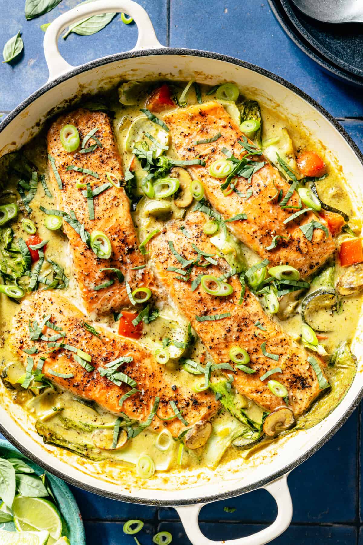 Thai-Inspired Coconut Green Curry Salmon in white skillet on blue tile background.