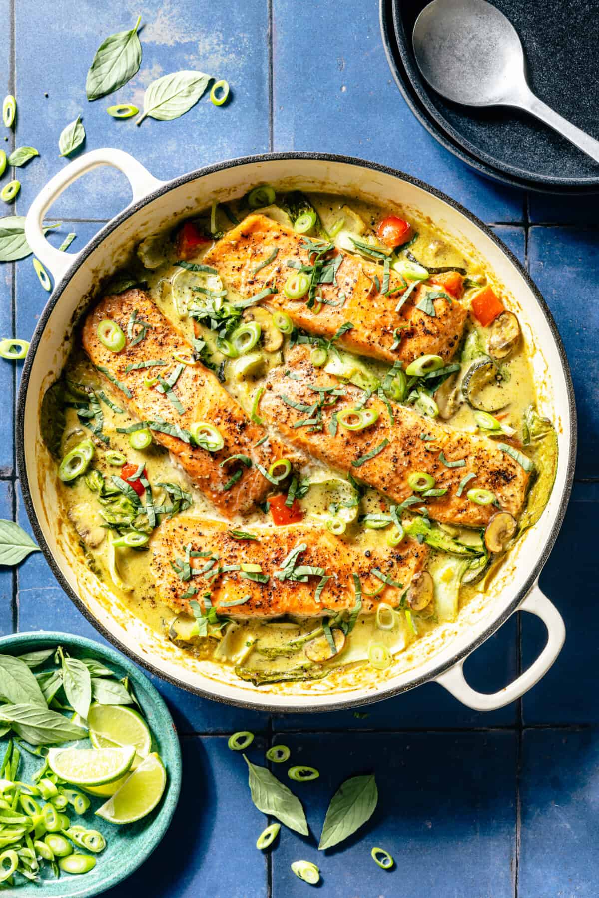 Thai-Inspired Coconut Green Curry Salmon in white skillet on blue tile background.