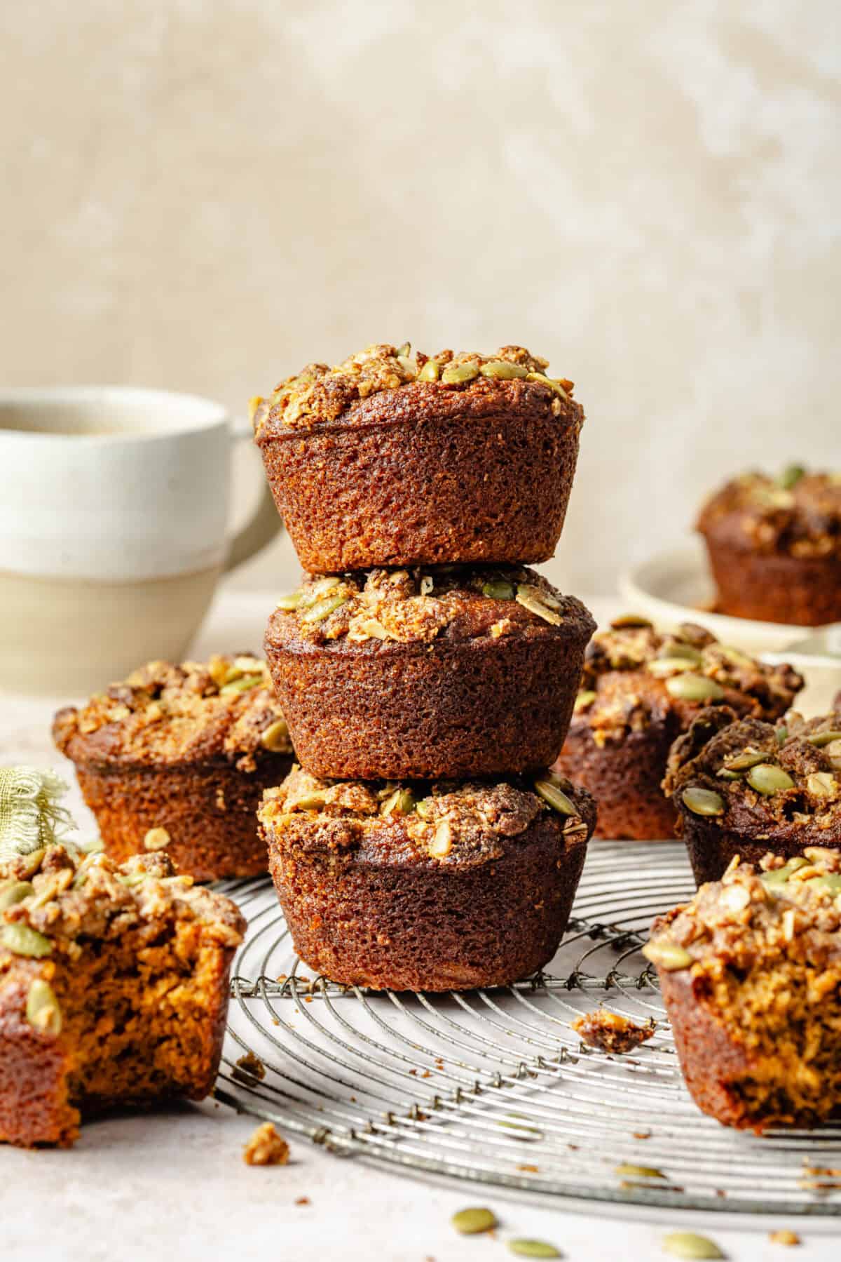 a stack of pumpkin muffins topped with pepitas and streusel on a neutral background