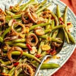 an up-close shot of green beans tossed with crispy shallots, garlic, and Calabrian chiles on a green toile platter