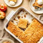 slices of apple dump cake on neutral plates with a bowl of whole cinnamon sticks and apples on the side