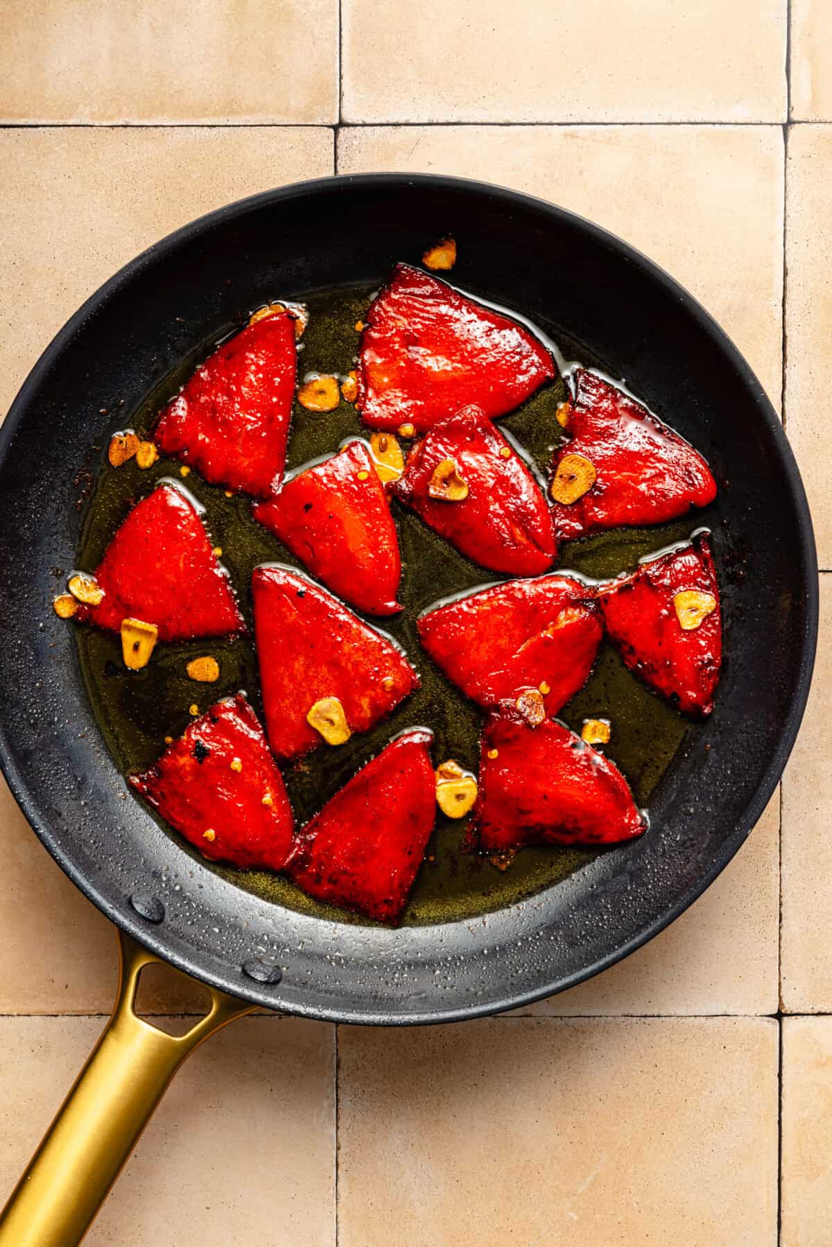 a dark skillet on a light tiled background with red peppers and garlic