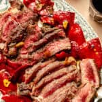 an up-close photo of seared rib eye steak with red peppers and garlic