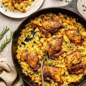 a cast-iron skillet with seared chicken thighs, orzo, vegetables, and fresh herbs