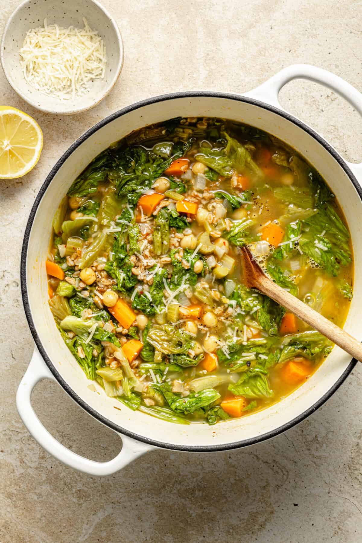 a large white dutch oven with chickpea and farro soup with a half lemon and grated cheese