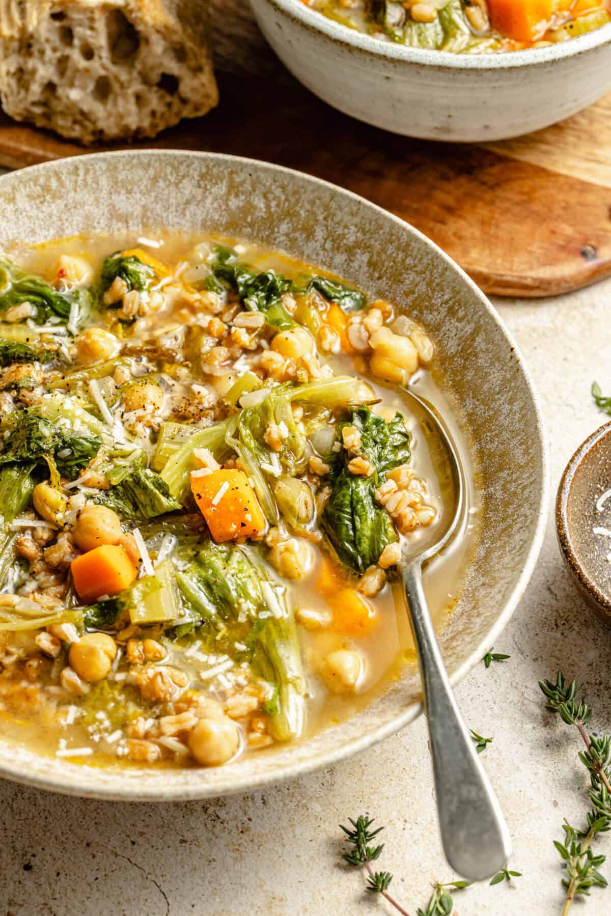 a large light tan bowl featuring chickpea and farro soup with fresh herbs