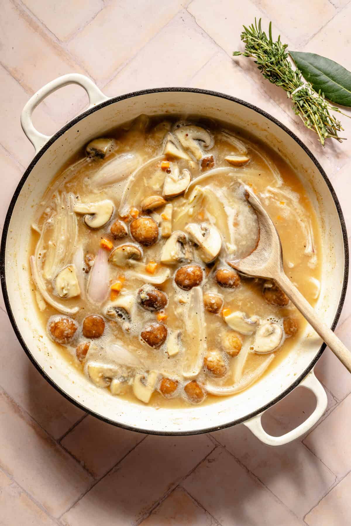 a large white Dutch oven on a light pink background featuring chicken and vegetables in a light broth