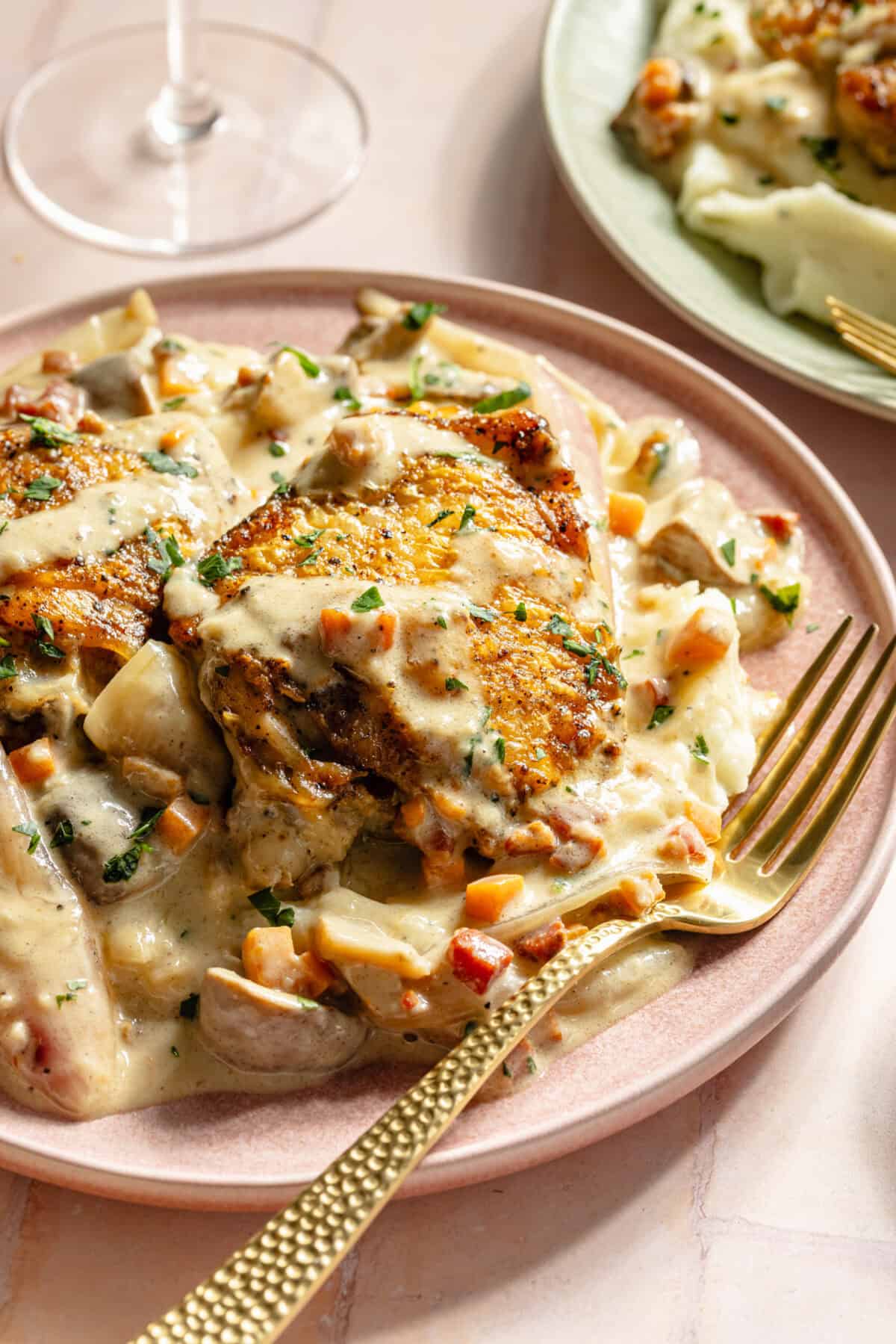 a light pink plate with chicken, a champagne sauce, and gold fork