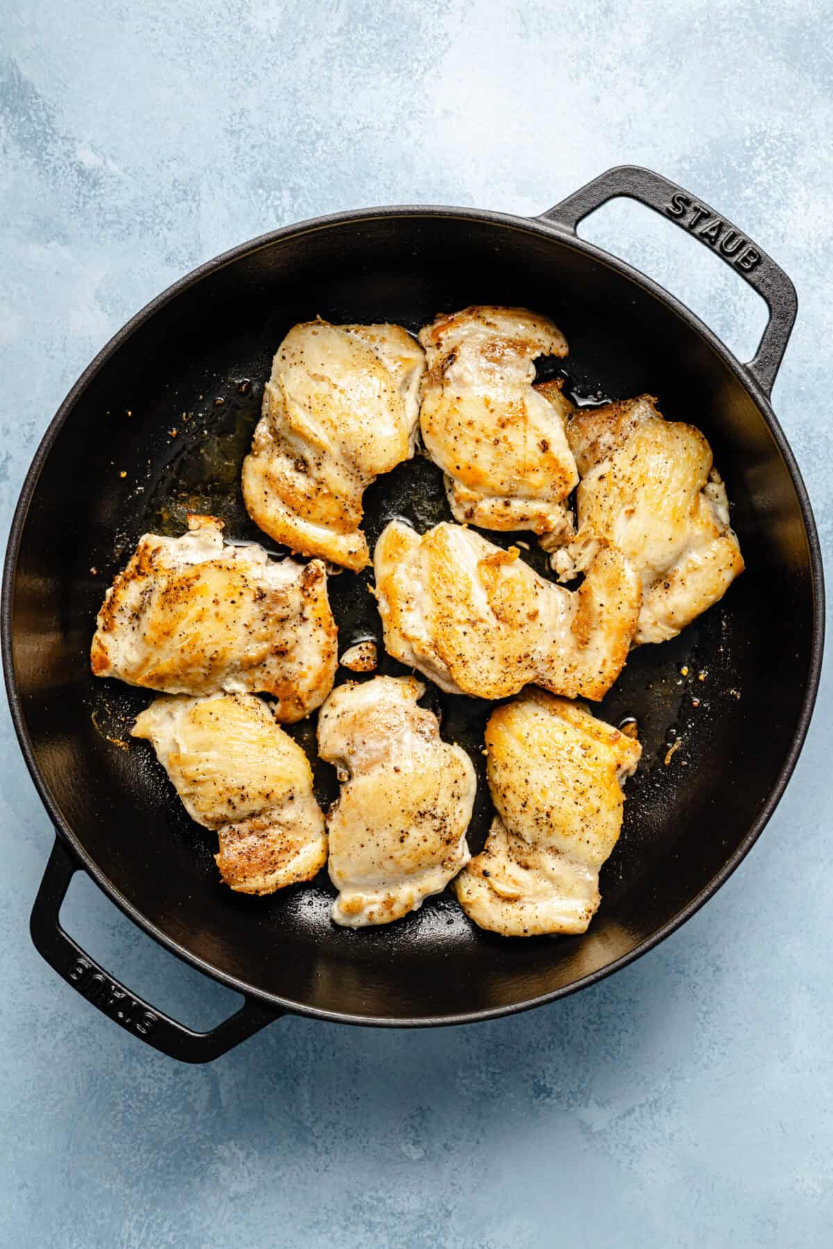 a large cast-iron skillet with bone-in skin-on chicken thighs on a light blue background